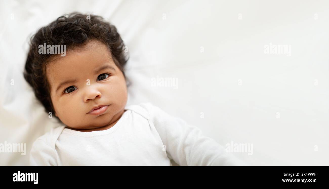 Portrait of cheerful curly sweet black little child boy or girl in clothes  lies on white bed in bedroom, close up Stock Photo - Alamy