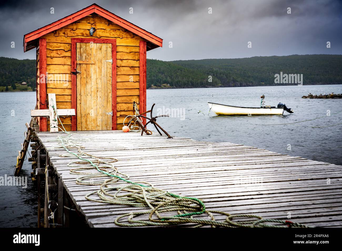 Fishing tackle shack on a wooden dock overlooking a small bay with fishing boats on the Atlantic Ocean under a stormy sky near Heart's Content Newfoun Stock Photo