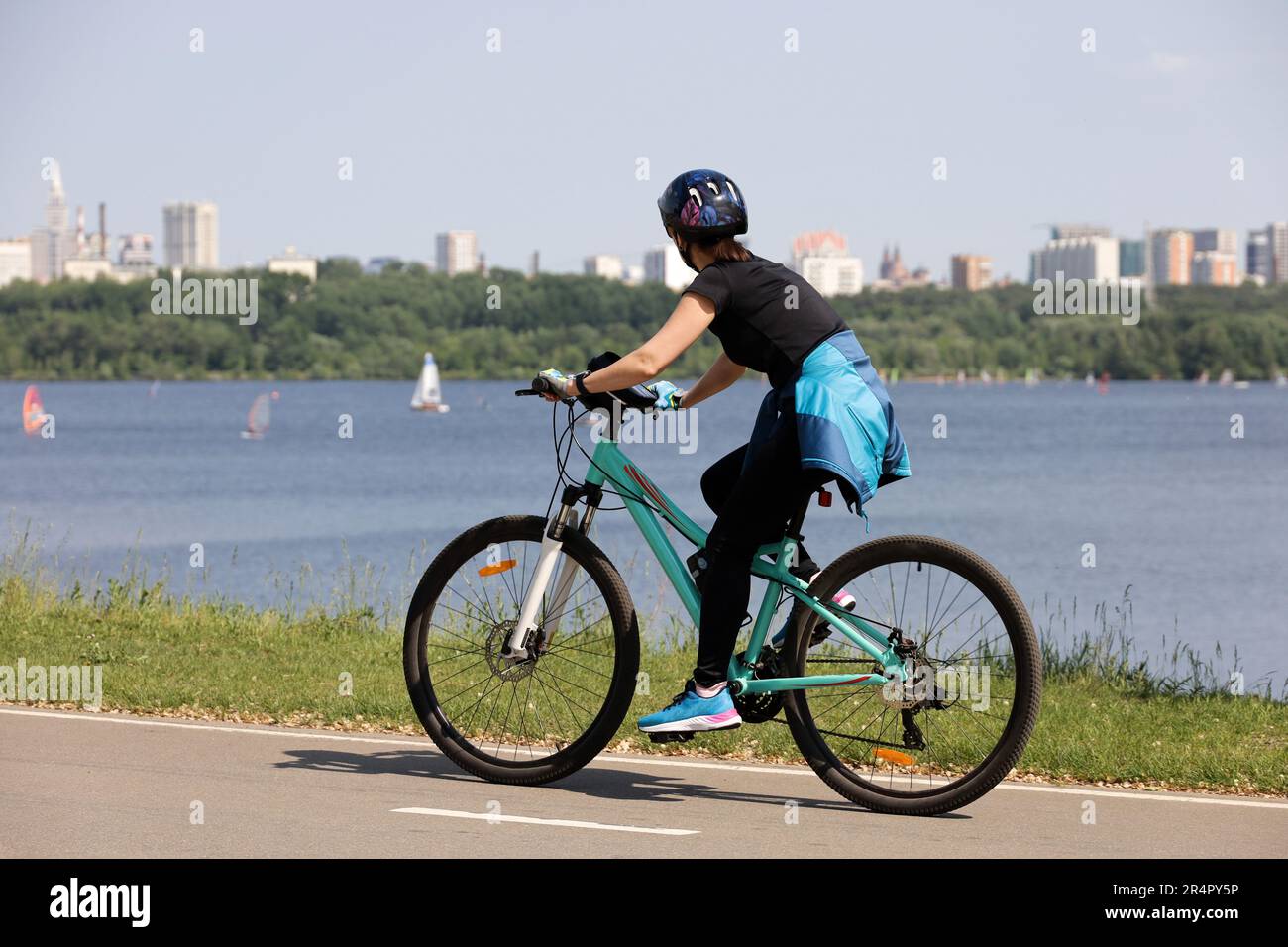 Girl in sportswear and helmet riding bicycle on river and city background. Cycling and summer leisure Stock Photo