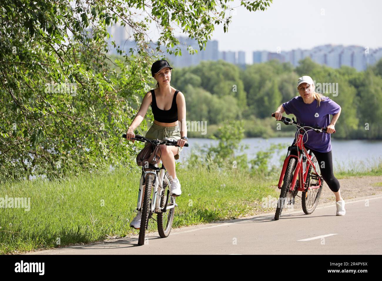 Cycling and leisure in city park. Two girls riding bicycles on river bank Stock Photo
