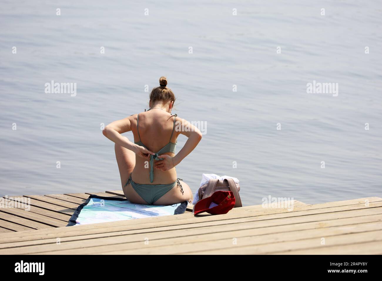 Beach vacation, girl fix her bikini sitting on wooden pier. Summer tan and leisure Stock Photo