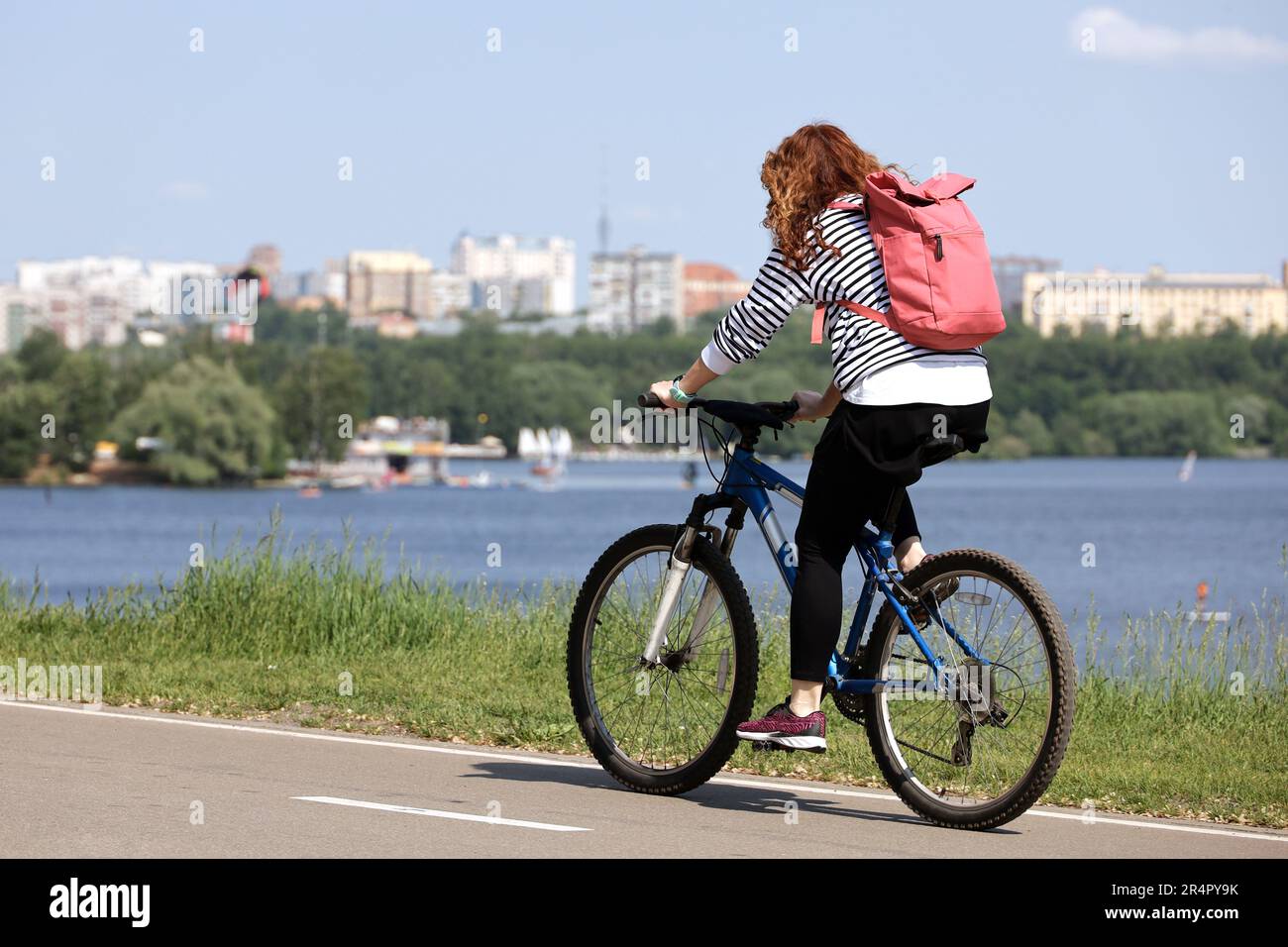 Woman tourist riding bicycle on river and city park background. Cycling and summer leisure Stock Photo