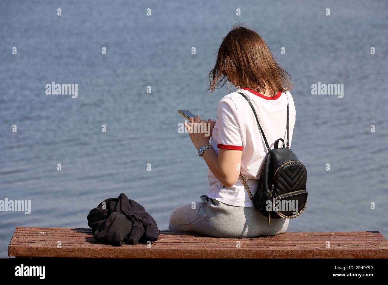 Girl sits on the beach with her smartphone in hands. Concept of online communication, summer leisure Stock Photo