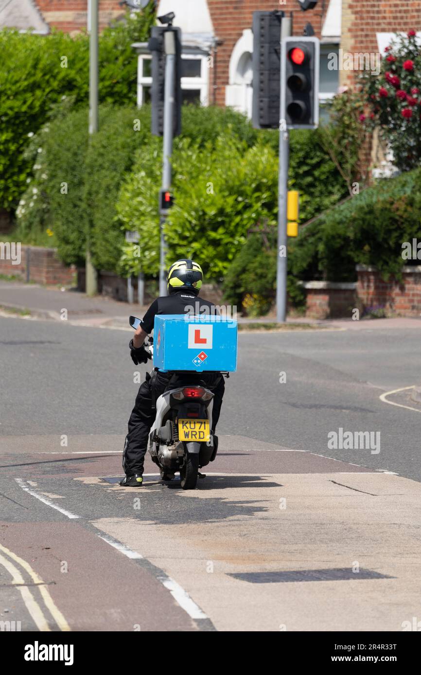 A moped rider with an L Plate delivering pizza for Dominos Pizza, Basingstoke, UK. Concept: fast food delivery, gig economy, trainee employee Stock Photo