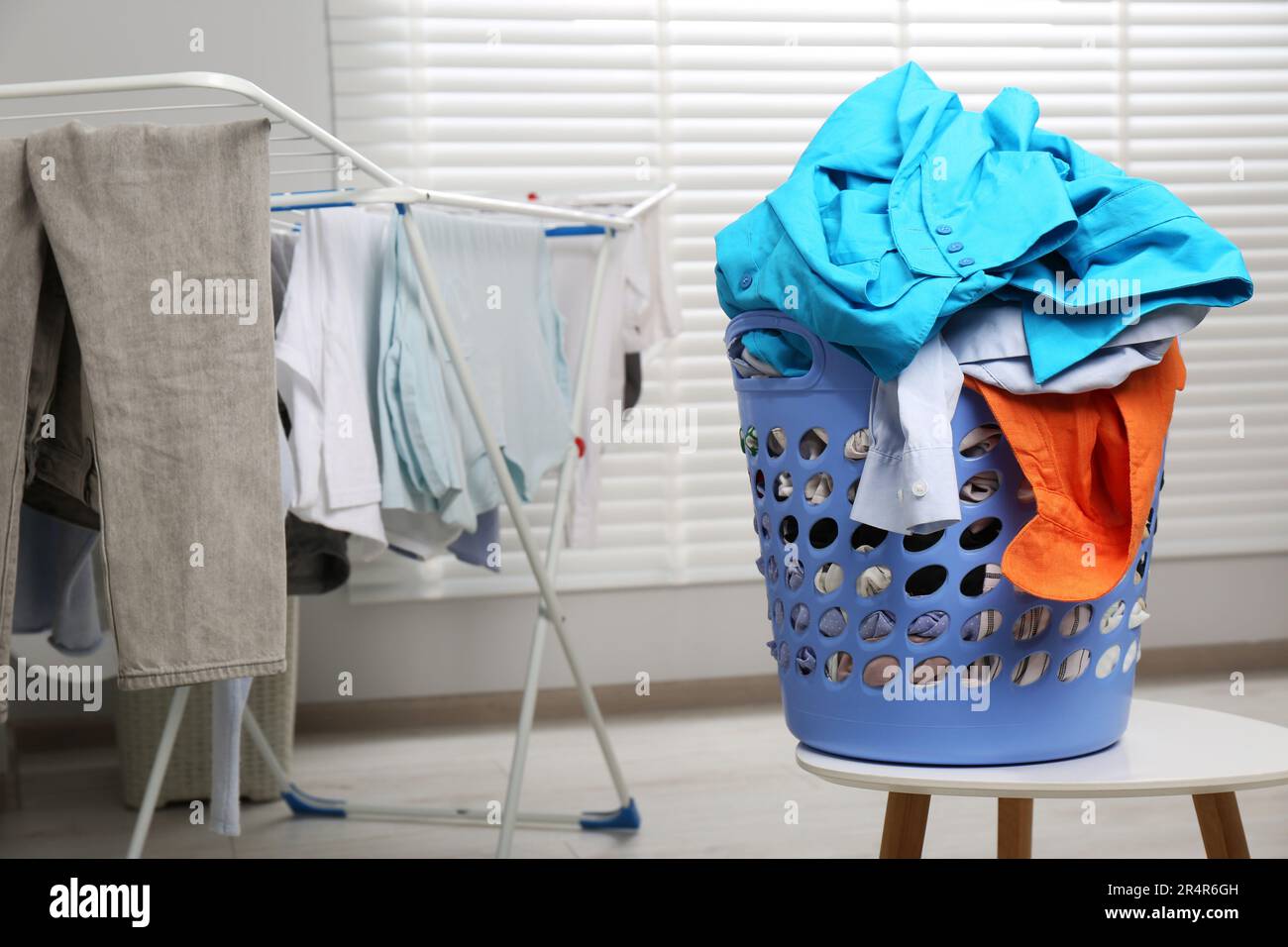 Plastic laundry basket overfilled with clothes near drying rack on