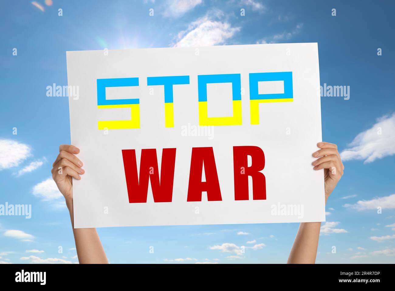 Woman holding poster with phrase Stop War against sky, closeup. Word Stop in colors of Ukrainian flag Stock Photo