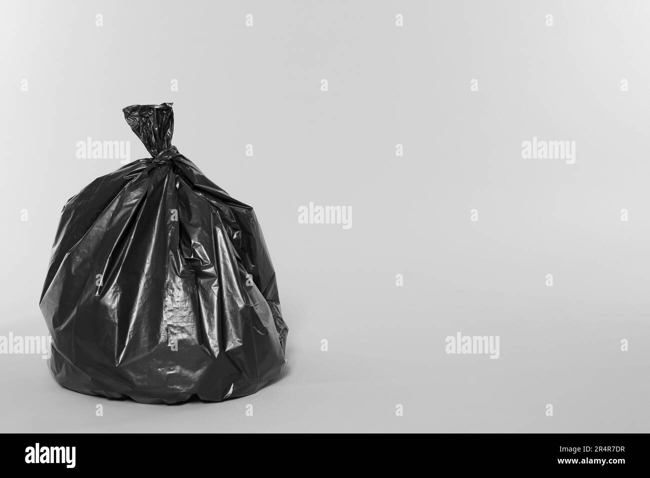 Trash bag full of garbage on light grey background. Space for text
