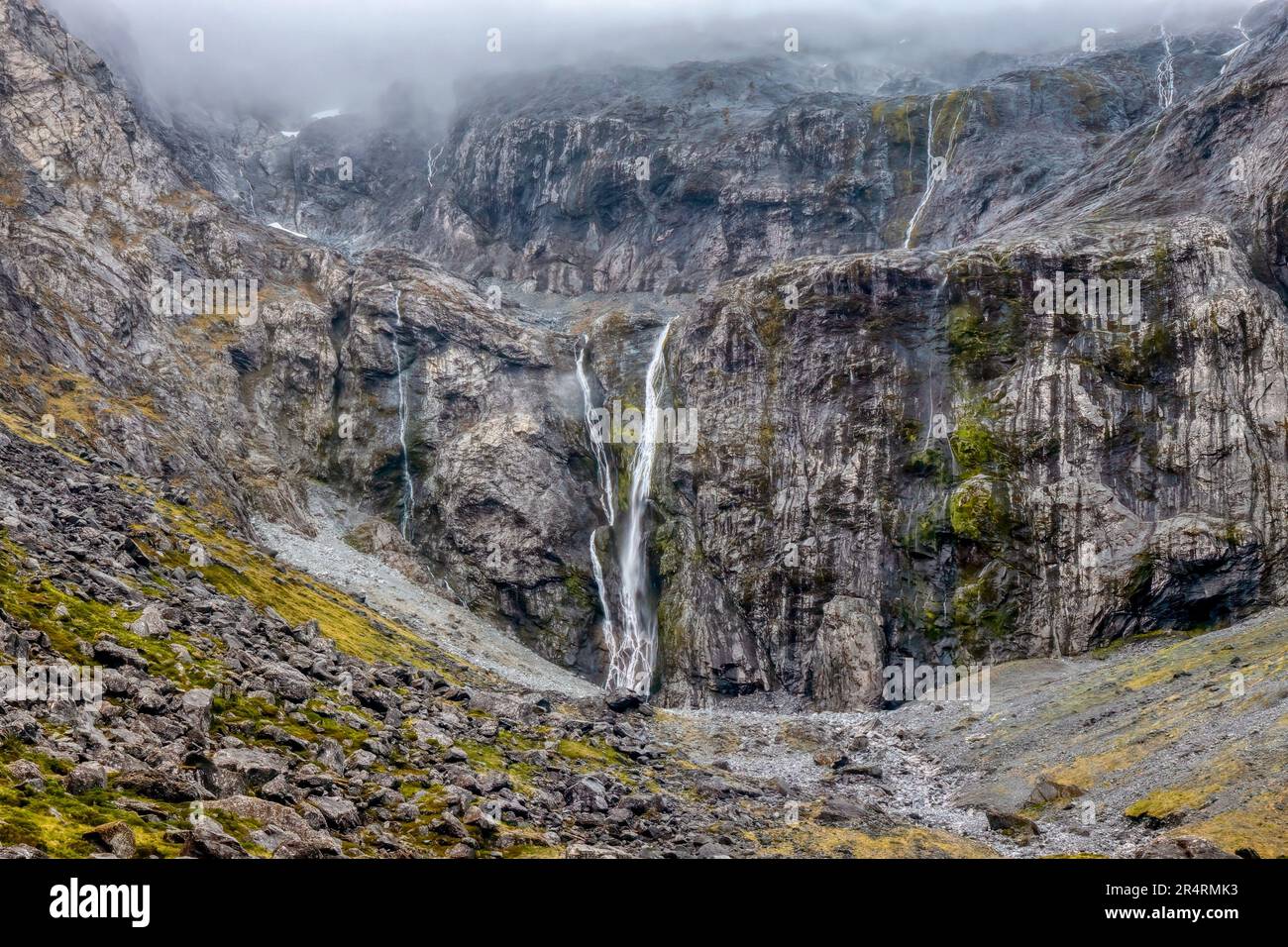 Waterfalls, mist and rain over a steep wall of granite on the South Island of New Zealand, near the entrance to the Homer Tunnel near Milford Sound. Stock Photo