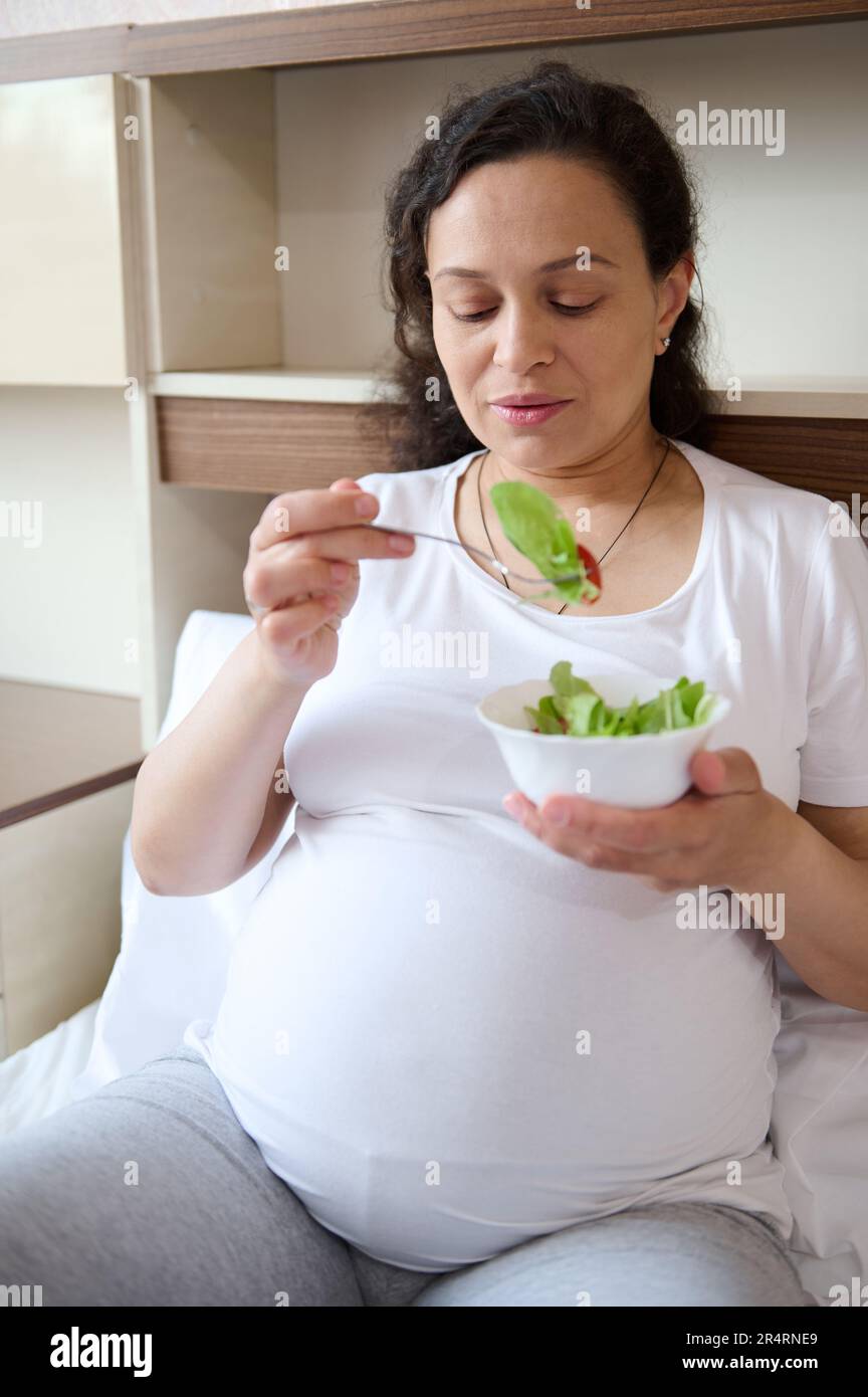 Pregnant woman in third trimester of her pregnancy, sitting on the bed