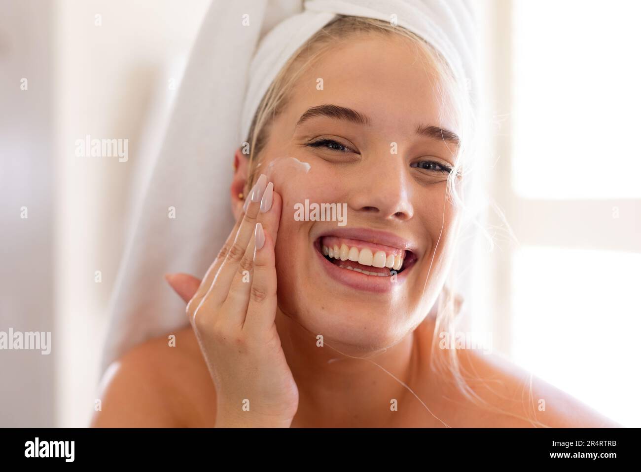 Closeup of plus size caucasian young woman with towel wrapped on head applying cream on face Stock Photo