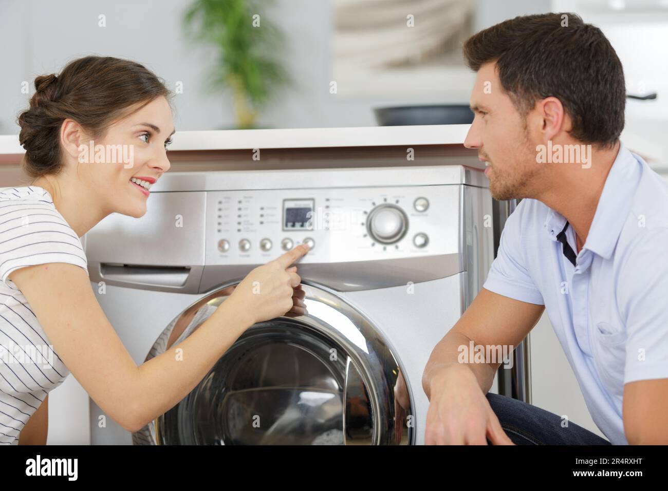 husband helping positive housewife to use washing machine indoors Stock Photo
