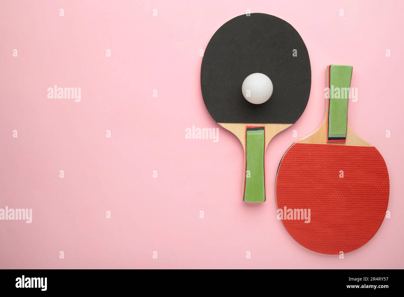 Ping pong rackets and ball on pink background with copy space. Top view