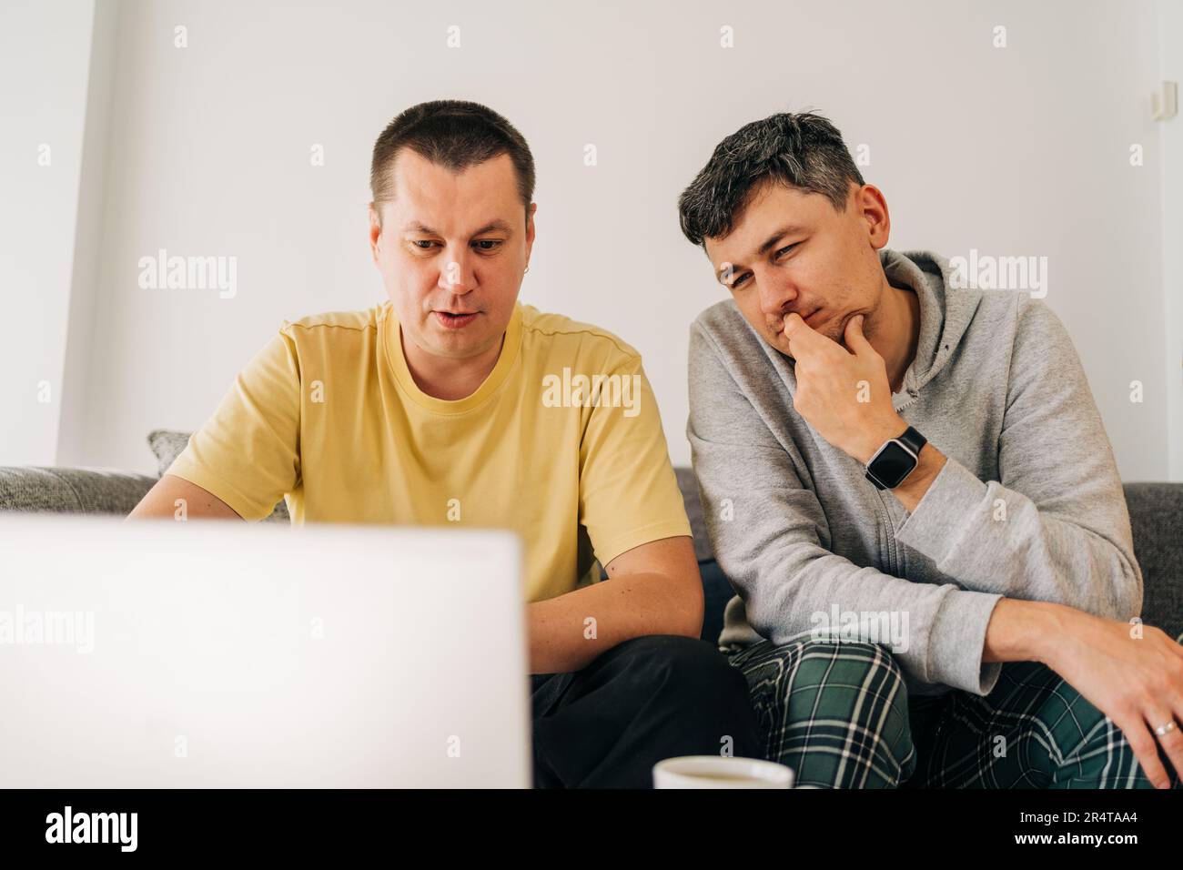 Two IT freelancer men typing in laptop working from home office. Two programmers sitting on couch doing code review. Distance learning online Stock Photo
