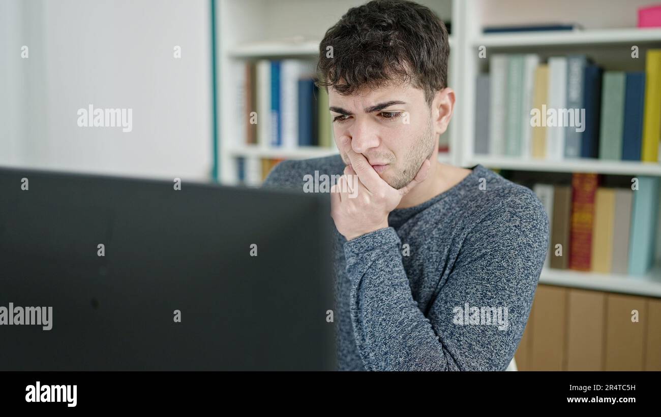 Young hispanic man using computer thinking at library university Stock Photo