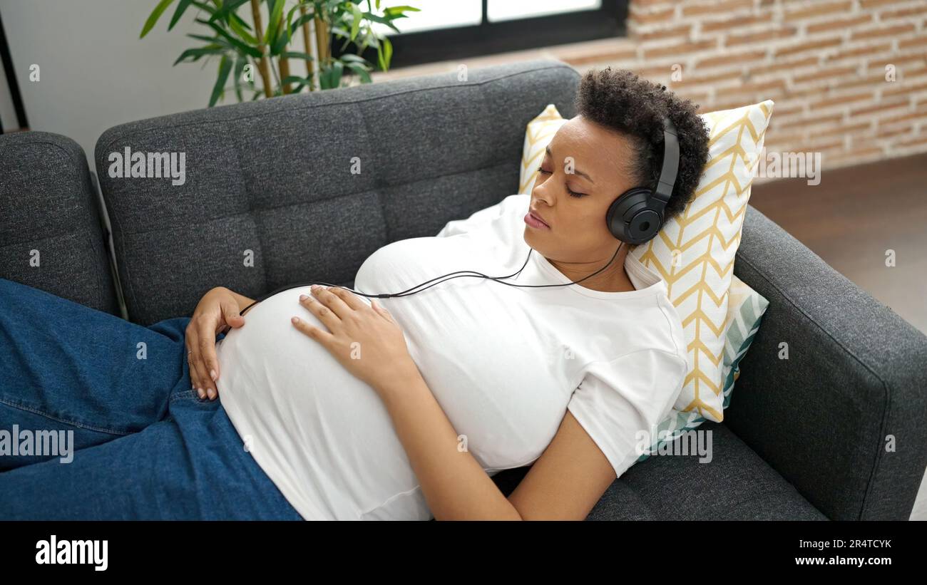 Young pregnant woman listening to music sleeping on sofa at home Stock ...