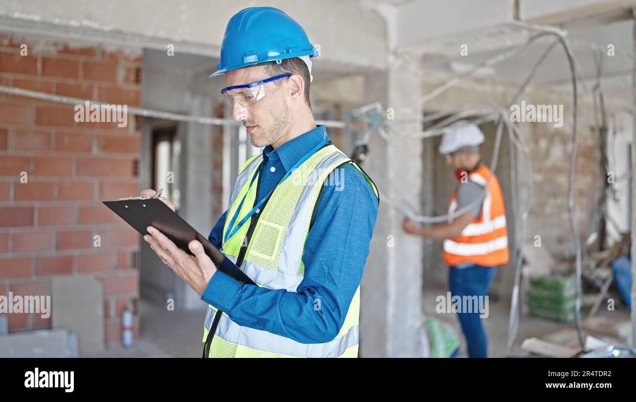 Two men builders writing document working at construction site Stock Photo