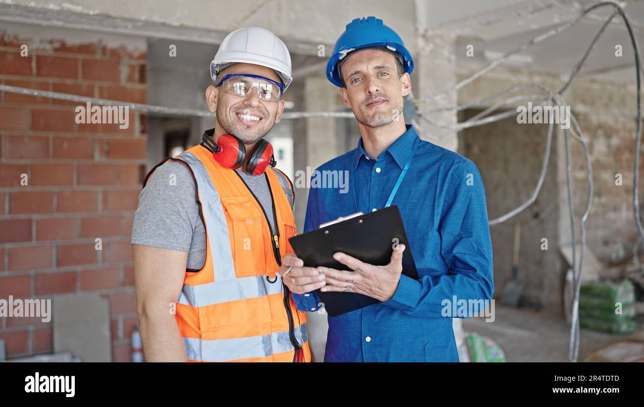 Two men builder and architect smiling confident writing document at construction site Stock Photo