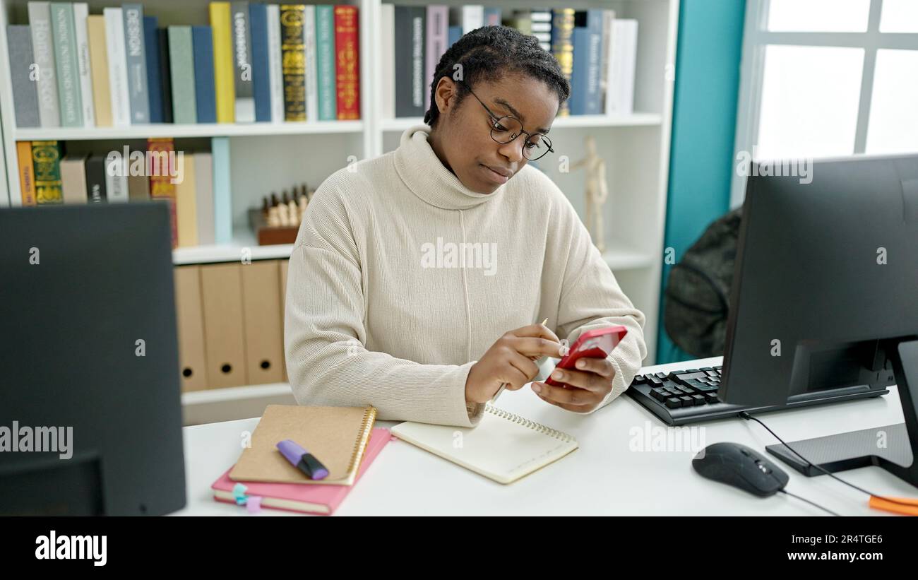 African american woman student using computer and smartphone at library ...