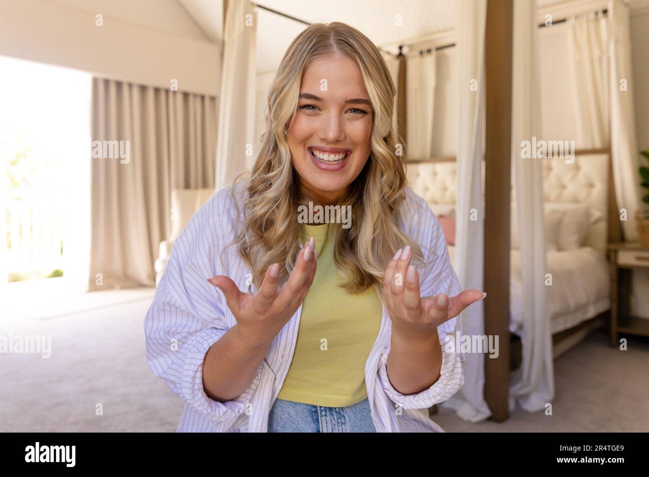 Blonde plus size caucasian young woman gesturing and looking at camera while sitting in bedroom Stock Photo