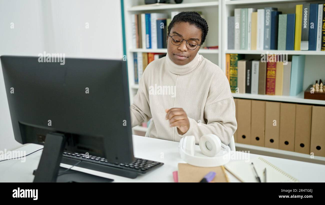 African american woman student using computer looking headphones at ...