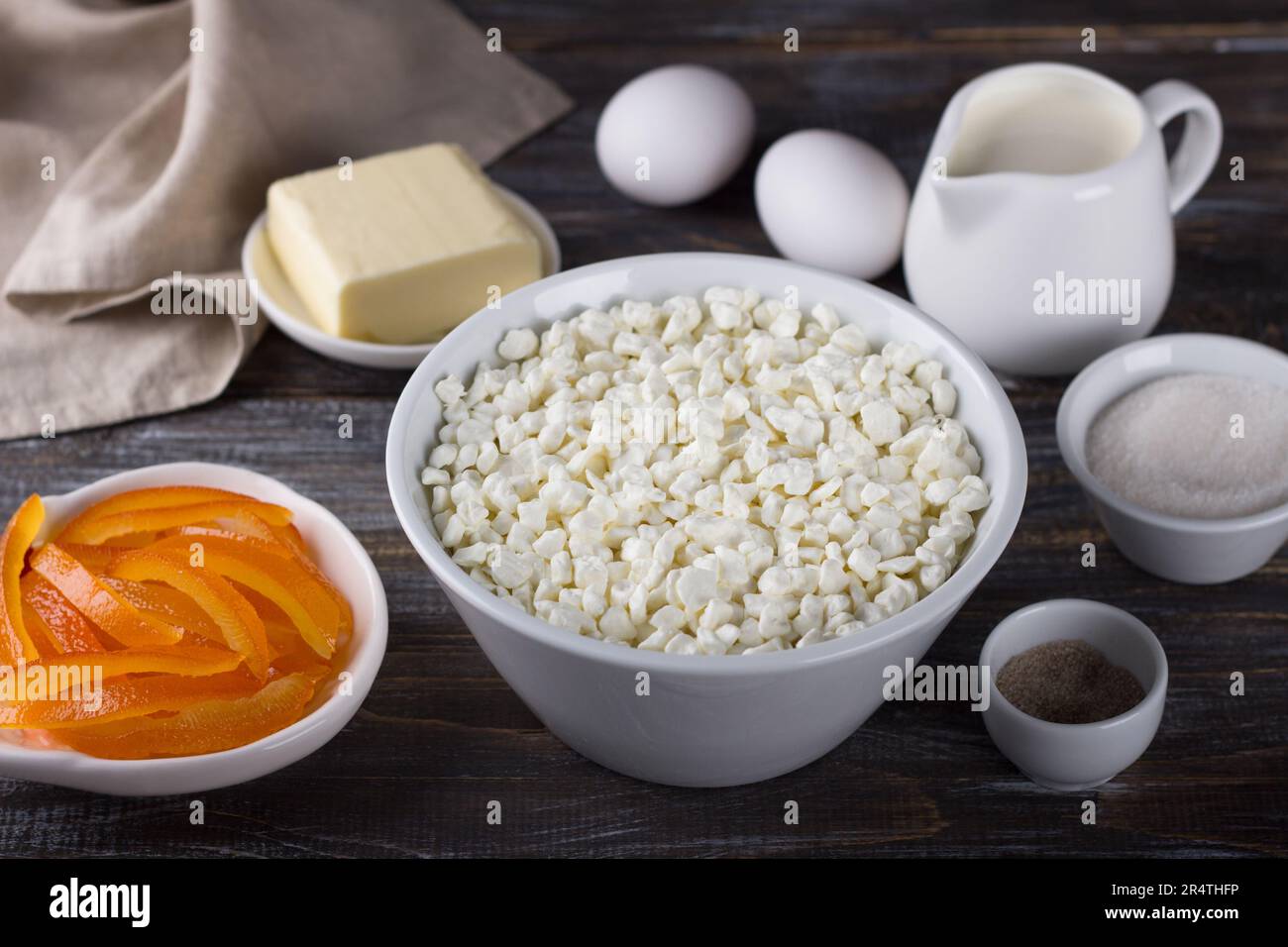 Bowl with cottage cheese, candied oranges, cream, eggs, butter, sugar, vanilla sugar on a wooden background. Ingredients for home baking Stock Photo