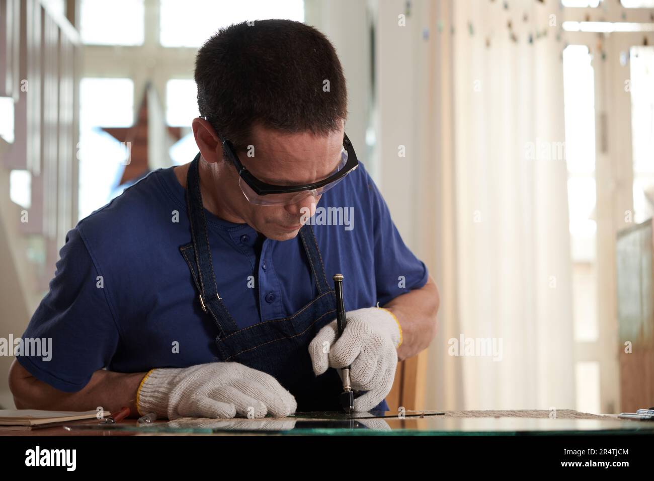 Concentrated craftsman in googles and textile gloves cutting mirror for ...