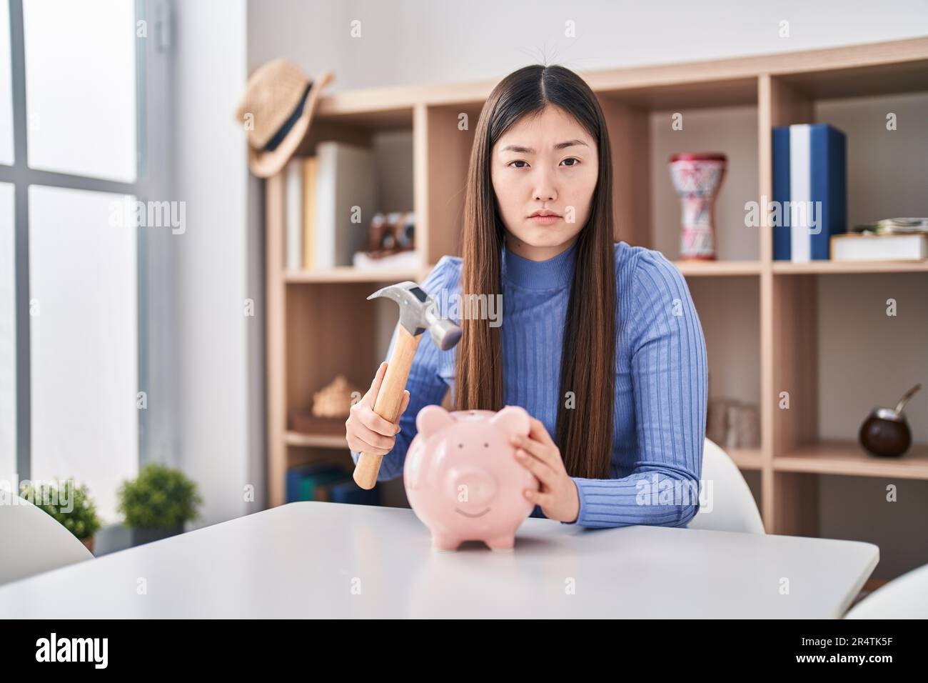 Chinese young woman holding hammer and piggy bank depressed and worry ...