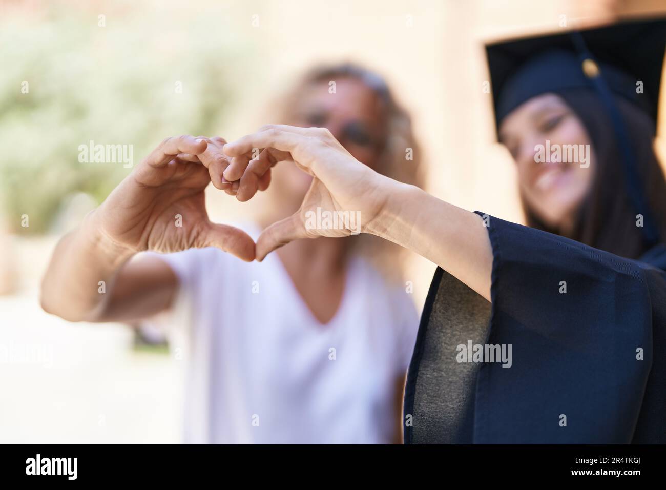 Two women mother and graduated daughter doing heart gesture with hands ...