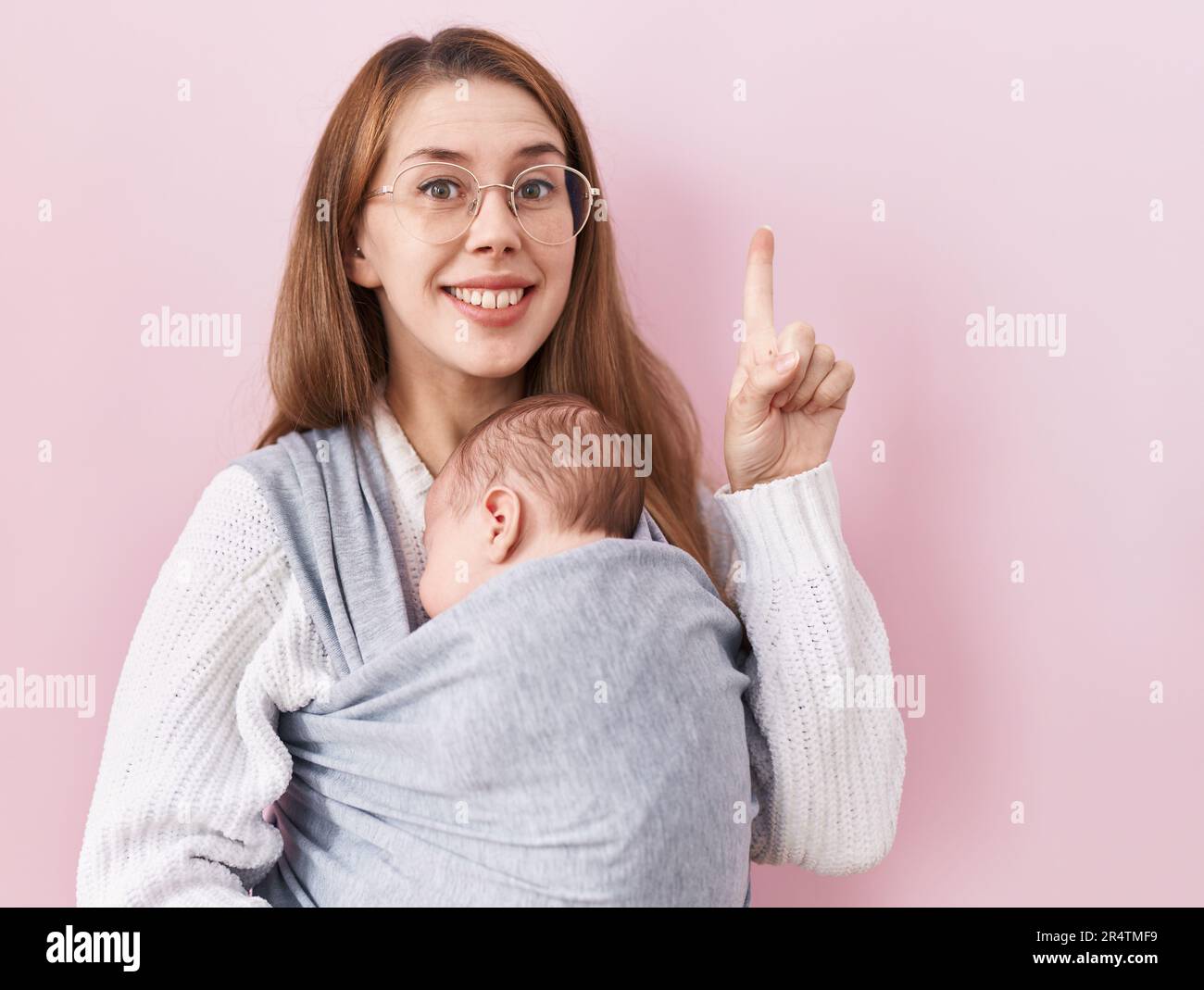 Young caucasian woman holding and carrying baby on a sling surprised with an idea or question