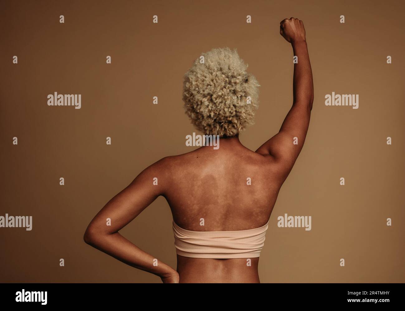 Woman confidently stands in the studio, her unique brown skin in monochrome with a brown background. Gen Z female raising her fist for women empowerme Stock Photo