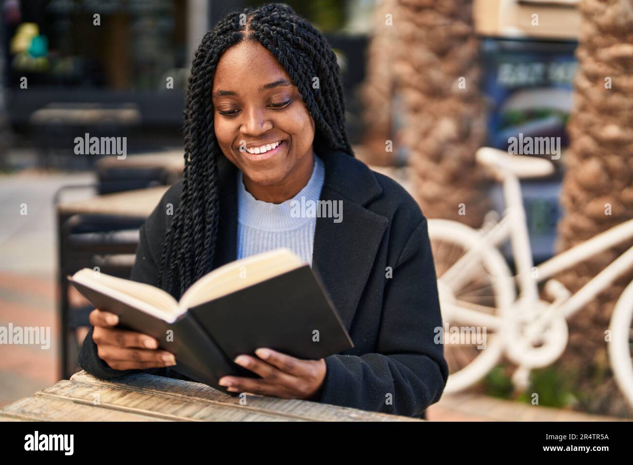 African american woman reading book sitting on table at coffee shop ...