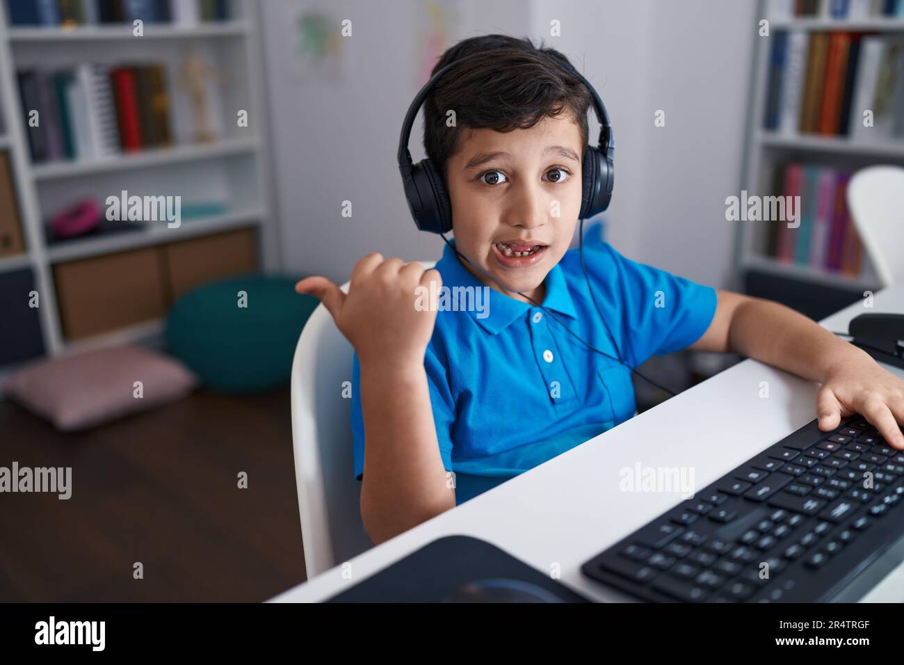 Little hispanic boy using computer laptop at the school pointing thumb ...