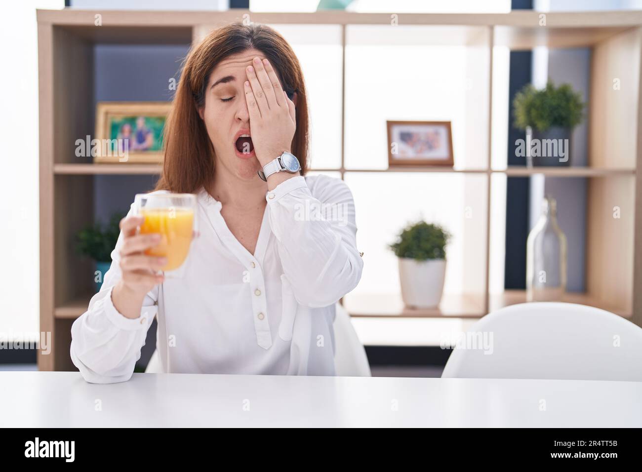 woman drinking glass of orange juice yawning tired covering