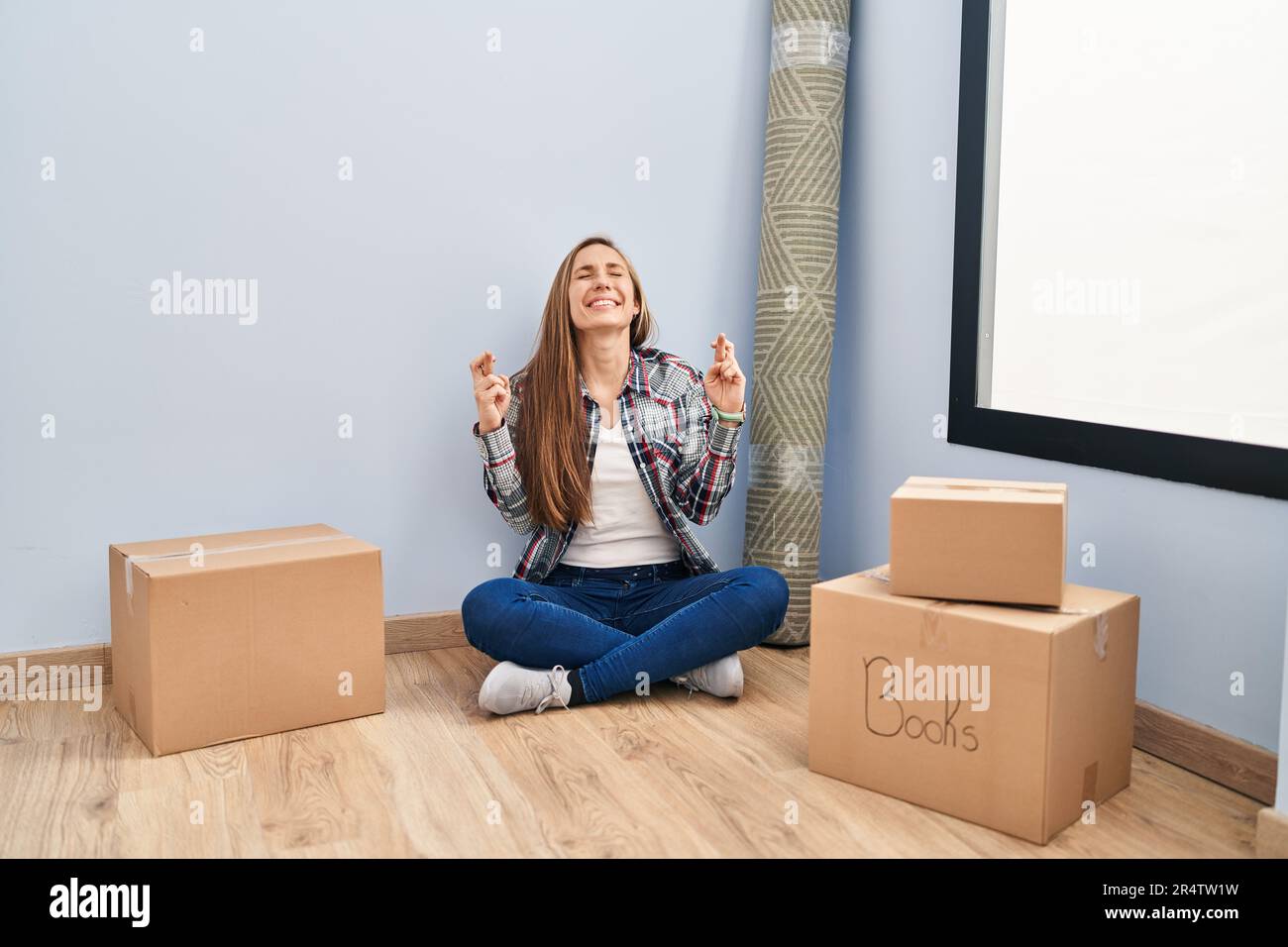 Young blonde woman sitting on the floor moving to a new home gesturing ...