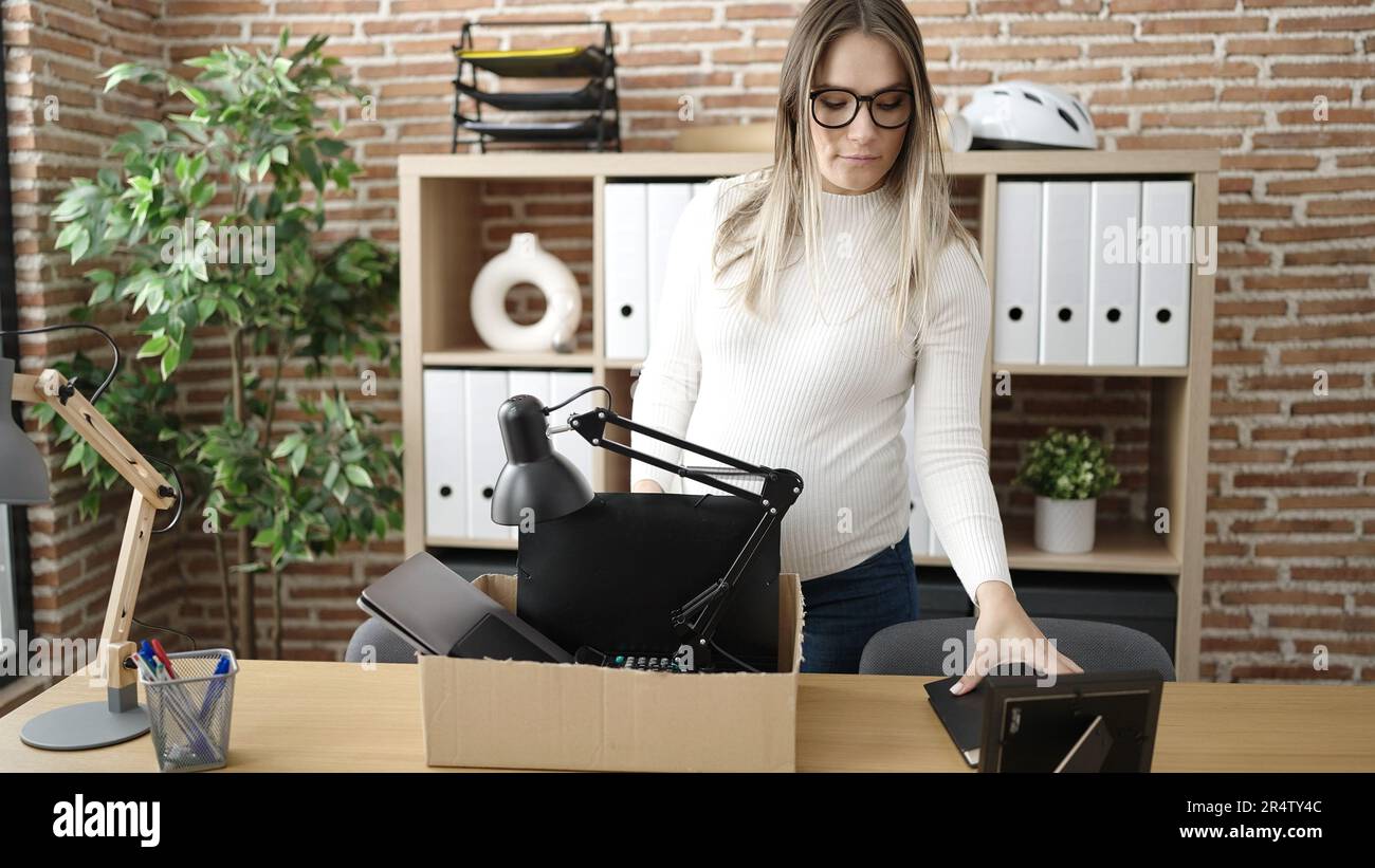 Young pregnant woman being fired packing belongings from workplace at office Stock Photo