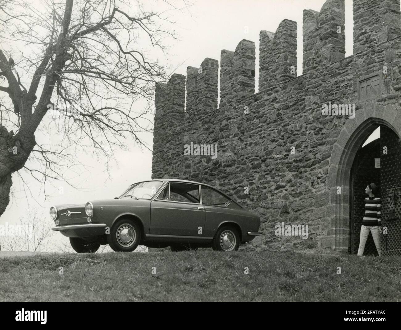 A woman and a FIAT 850 Coupè automobile getting out of a castle, Italy 1960s Stock Photo