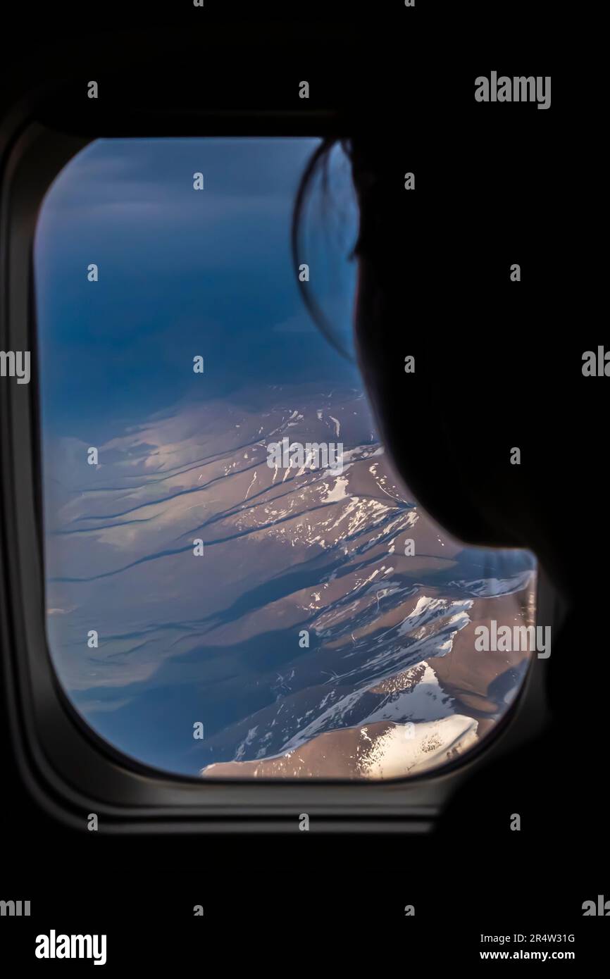 Silhouette of a person looking out an airplane window from her seat. Caucasus mountains - aerial night view from an airplane Stock Photo