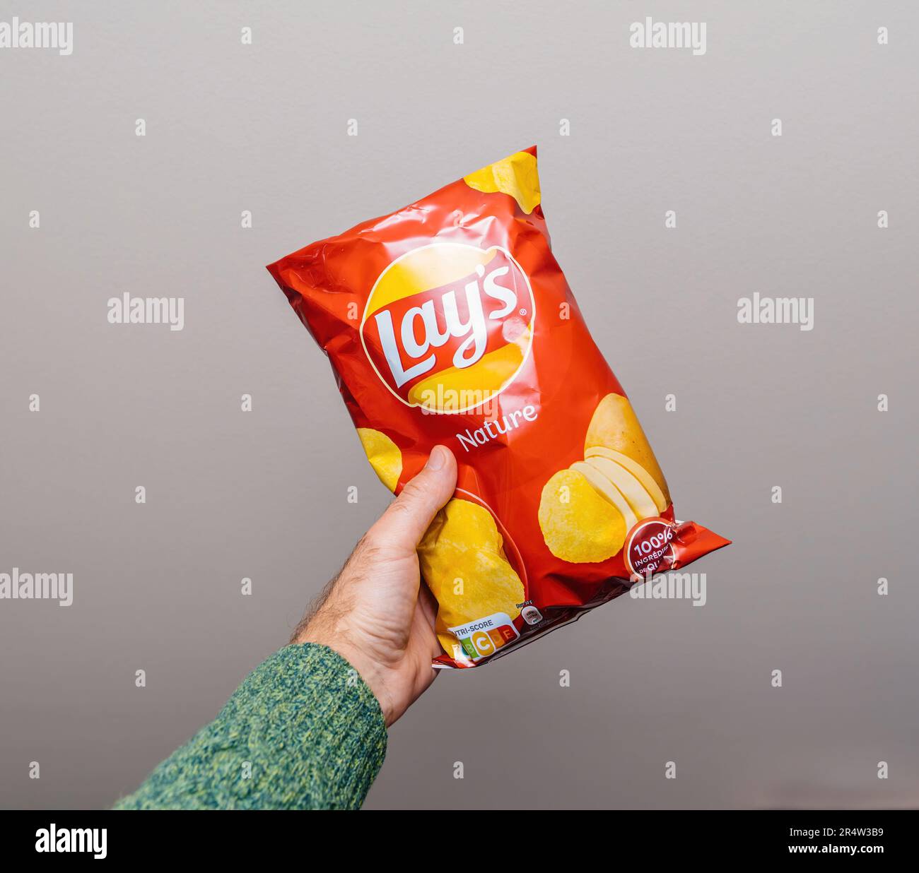 Lyon, France - May 24, 2023: A persons hand grasps a bright bag of Lays chips against an empty, gray background - delicious salt nature chips snack fo Stock Photo