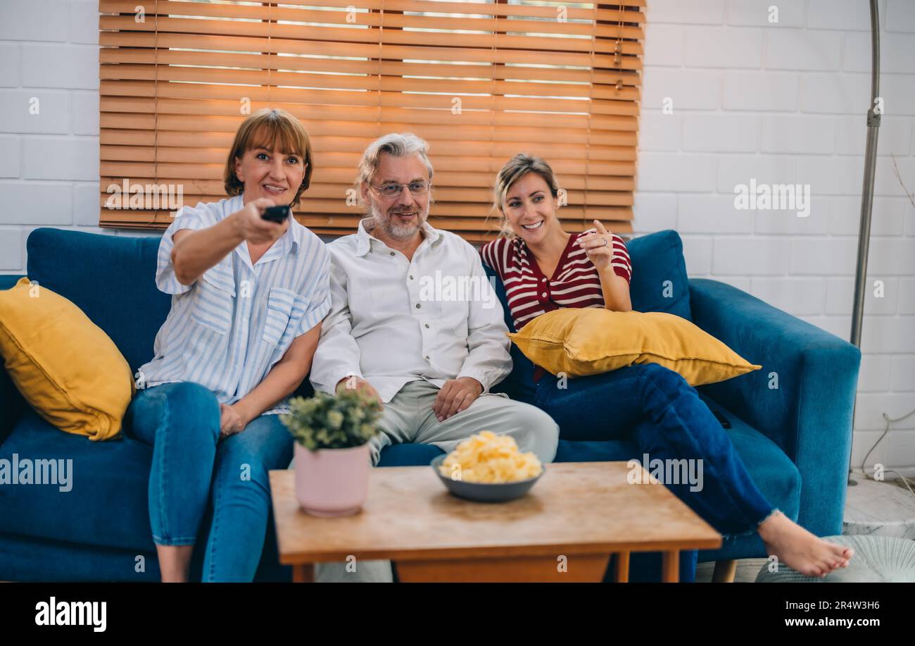 Members of the family from multiple generations enjoy quality time together by watching television, sharing snacks and conversation, discovering new a Stock Photo
