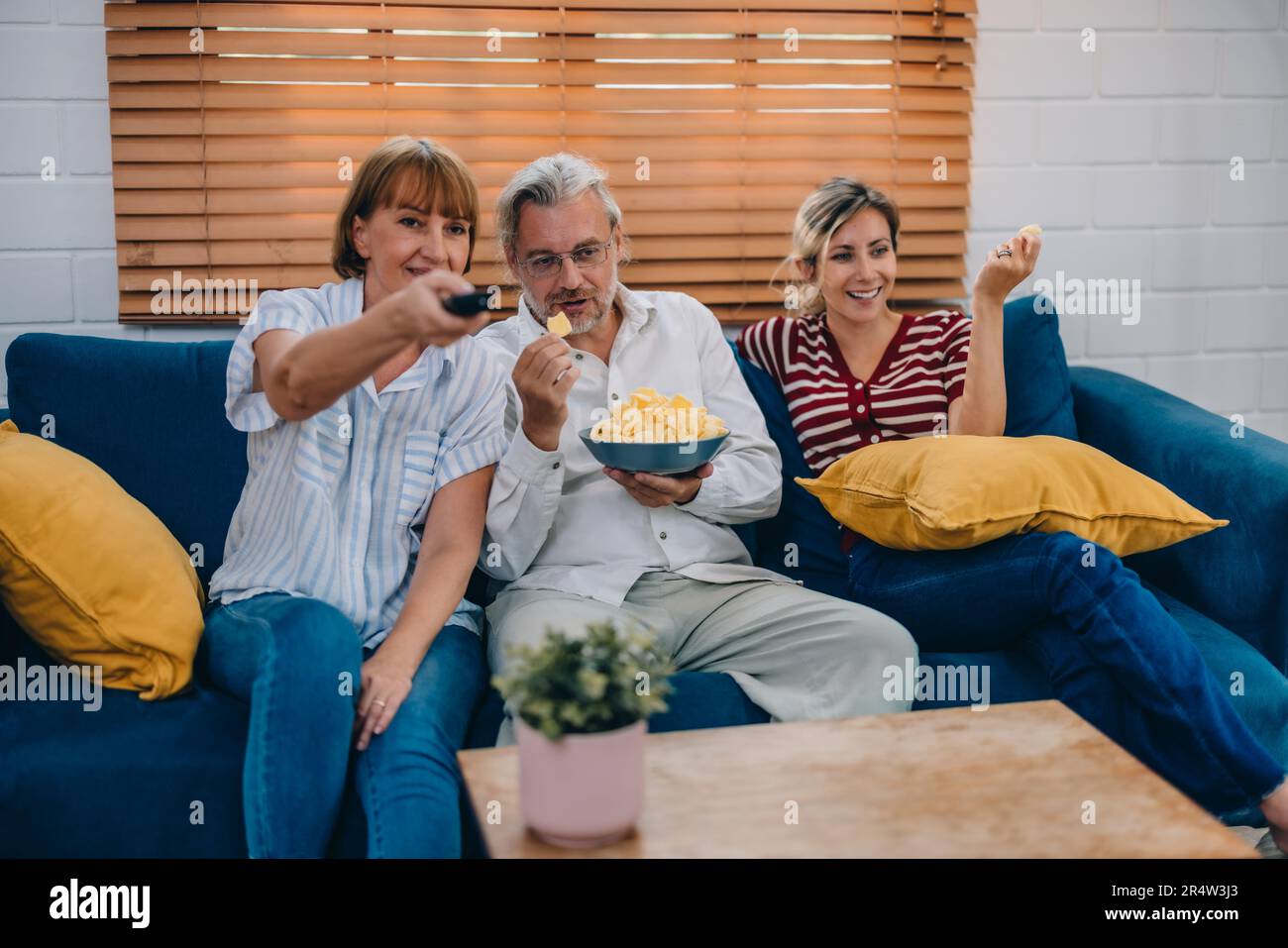 Members of the family from multiple generations enjoy quality time together by watching television, sharing snacks and conversation, discovering new a Stock Photo