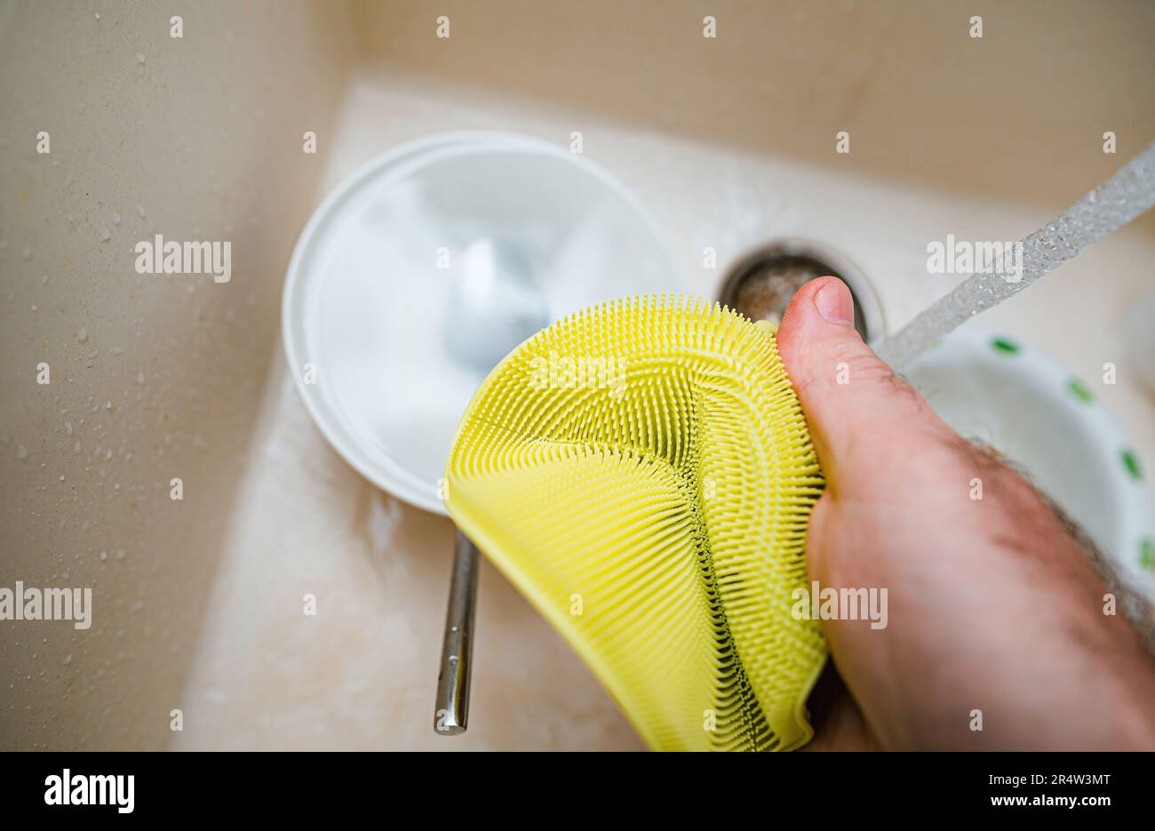 A person holds an yellow silicone sponge above a sink full of sparkling