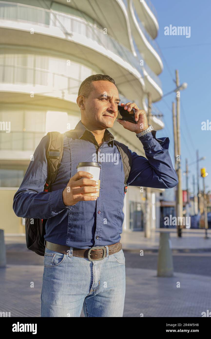 Young latin man talking on the mobile phone and holding a paper cup with coffee in his hand. Stock Photo