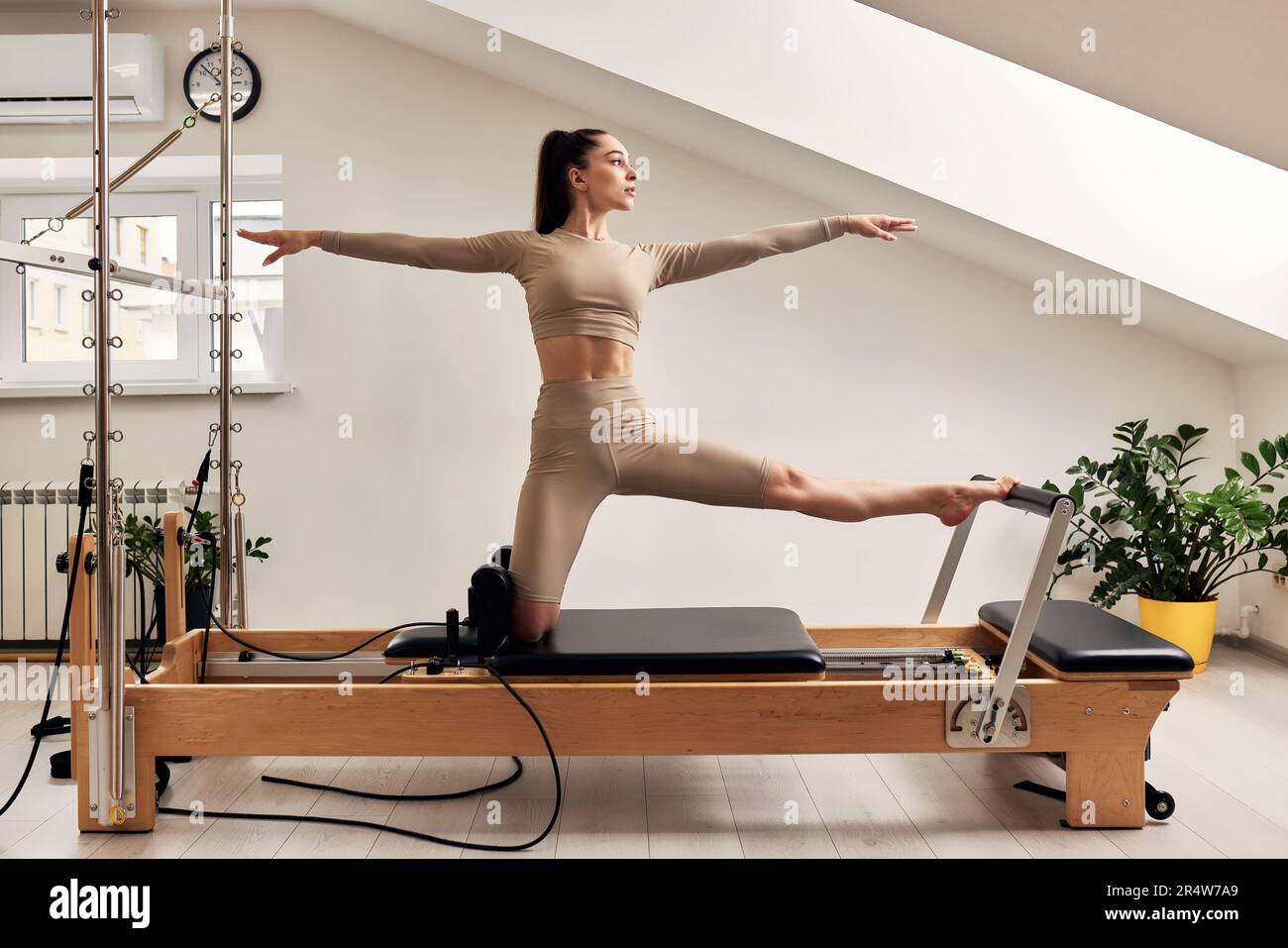 A young girl is doing Pilates on a reformer bed. A beautiful slender  brunette woman in a beige bodysuit is doing body strengthening and  stretching exe Stock Photo - Alamy