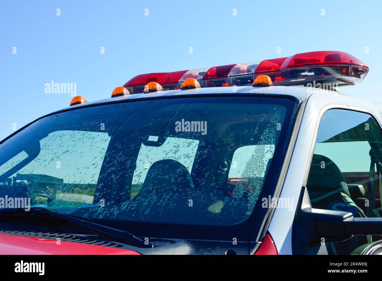 A red emergency firetruck with a lightbar on the roof. The lights are red, orange, and white color. The rescue pick-up truck has a white roof. Stock Photo