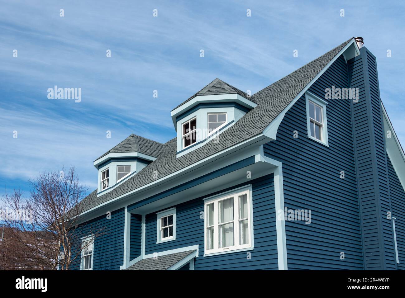 The exterior view of two polygonal dormers on a modern blue rooftop of a wooden house. The multi-sided dormers have three double-hung windows. Stock Photo