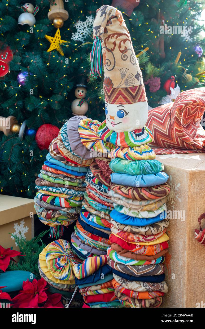 A vintage yo yo doll made of colorful quilting fabric below a decorated Christmas tree. The old toy has a cone for a hat with an embroidered clown Stock Photo