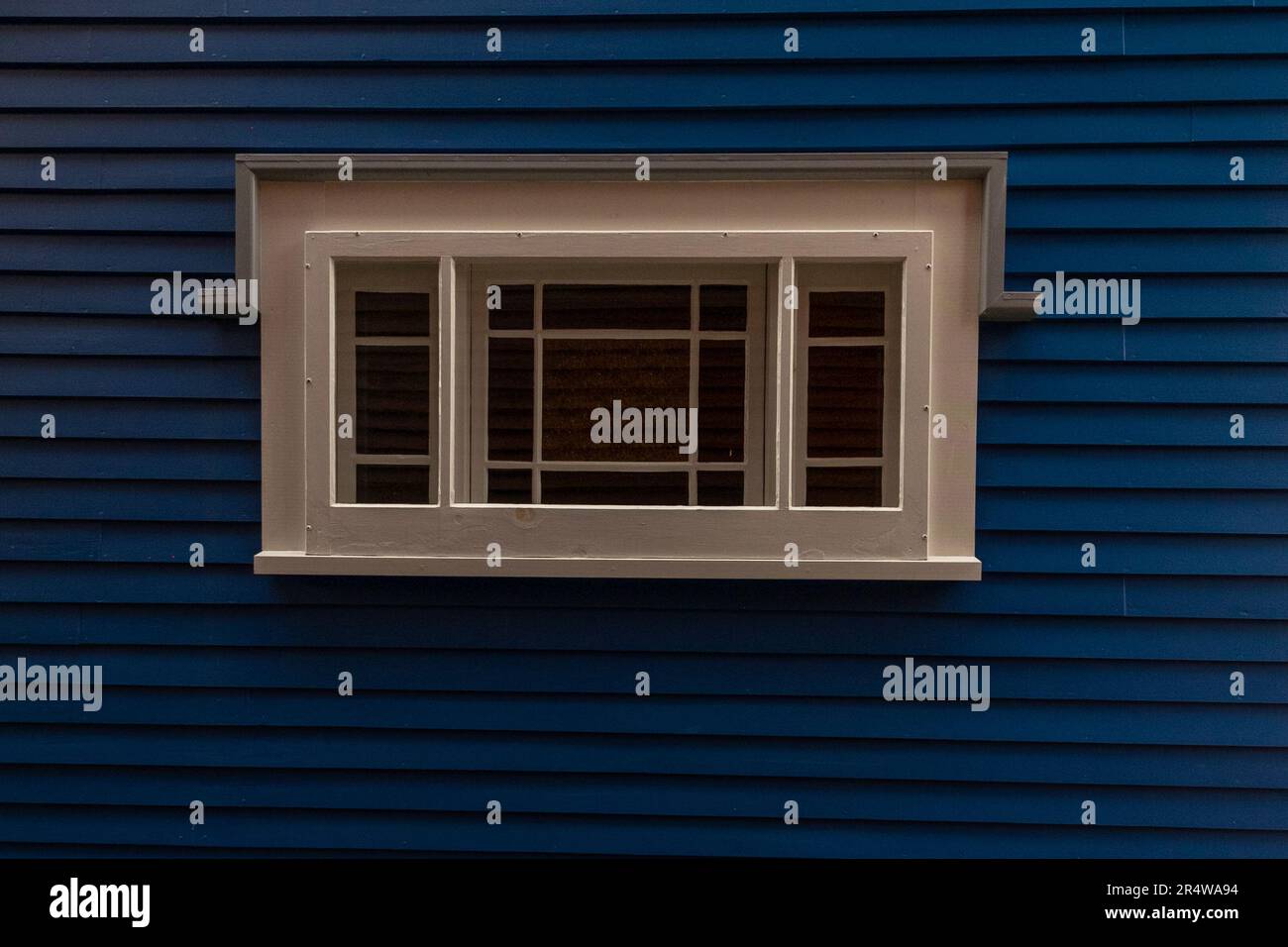 A navy blue painted exterior wall of a house with narrow clapboard siding and a vintage clear glass window with mullions between the panes. Stock Photo