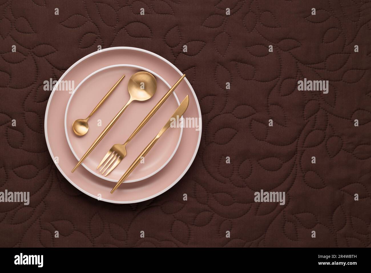 Set of golden cutlery and beige plates on dark table with brown fabric ...