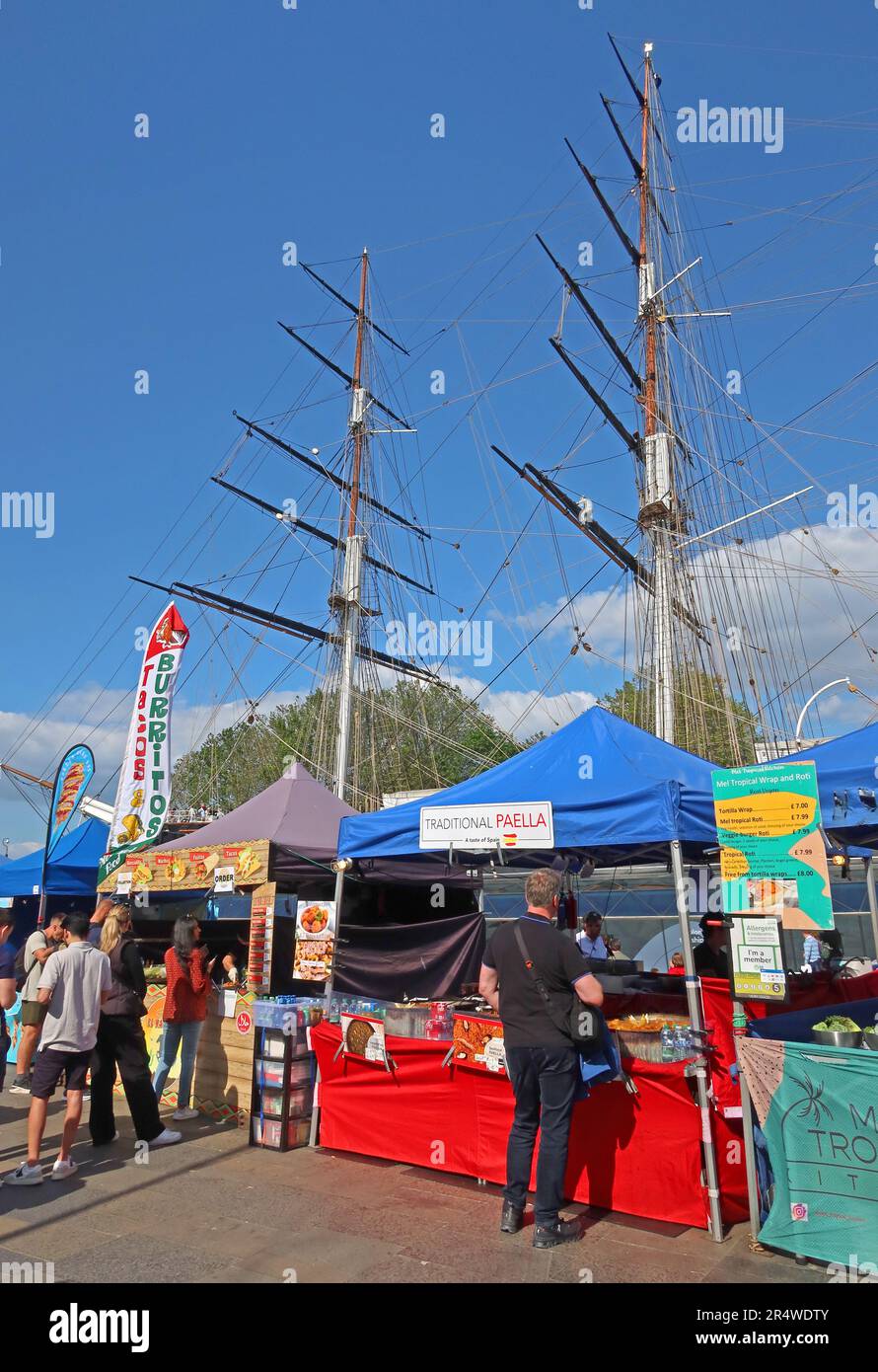 Street food stalls operating in Greenwich, London, with the masts of the Cutty Sark visible behind the market activity Stock Photo