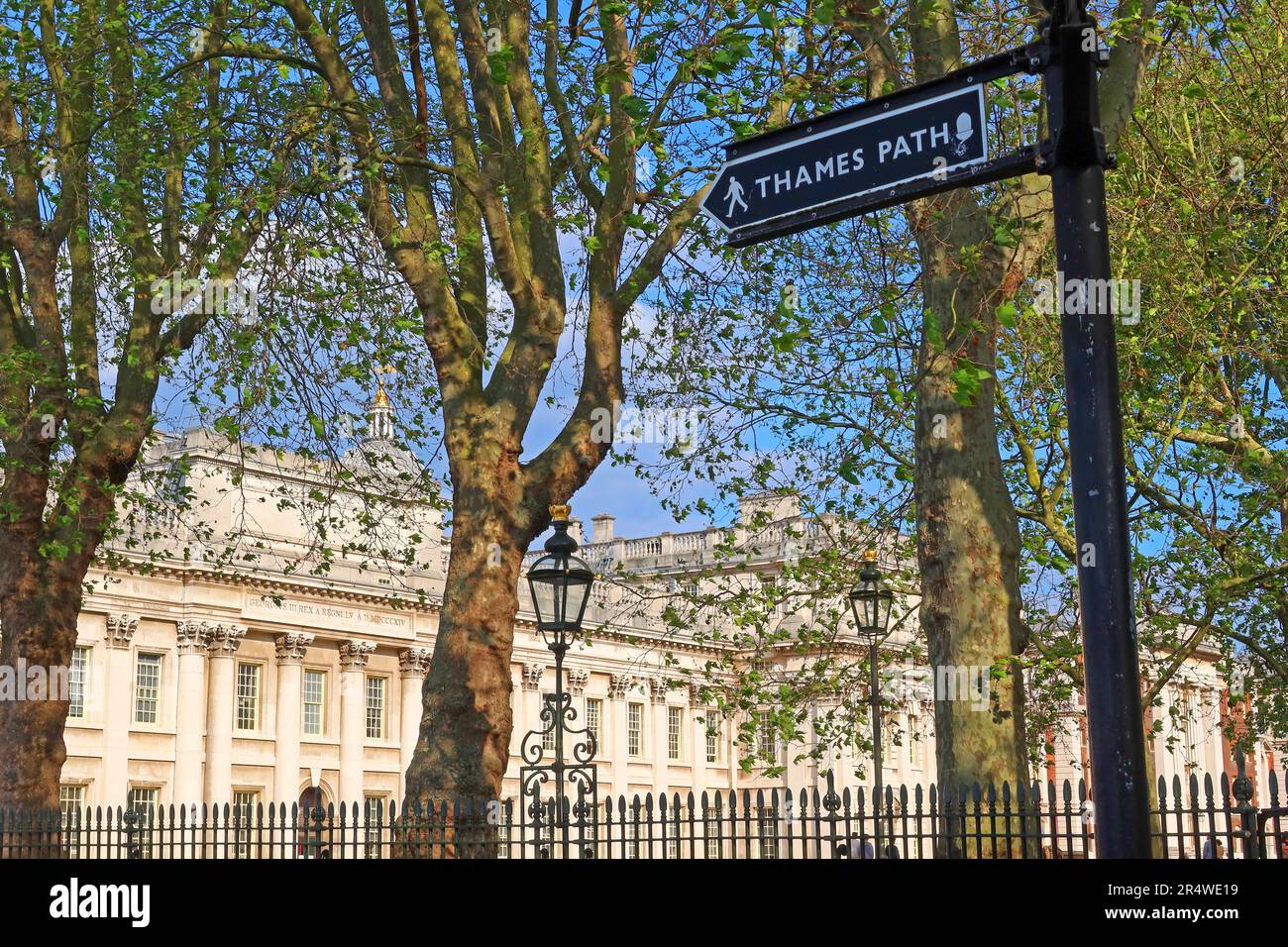 Thames Path signpost along the riverside in Greenwich, London, with historic buildings visible through trees in the background Stock Photo